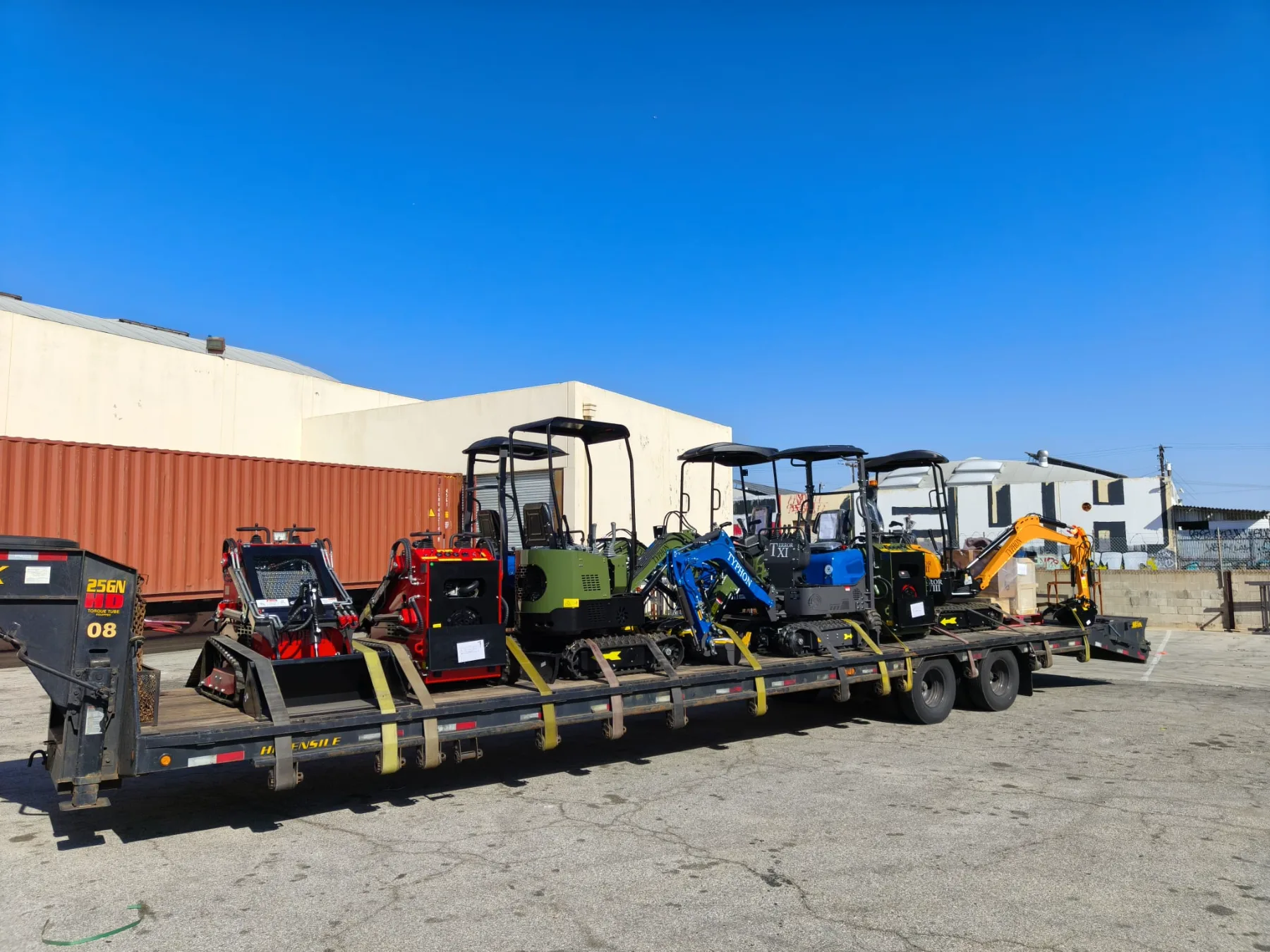 Heavy-duty ratchet straps securing mini machines to trailer bed